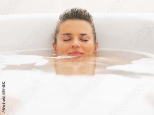 Young woman laying under water in bathtub