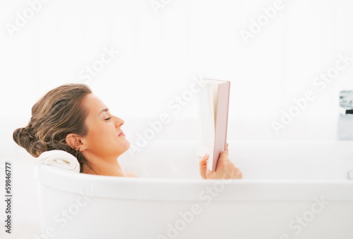 Young woman reading book in bathtub