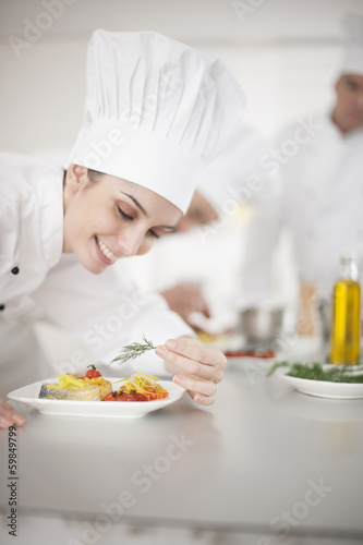 closeup on a female chef preparing a dish her team in the backg
