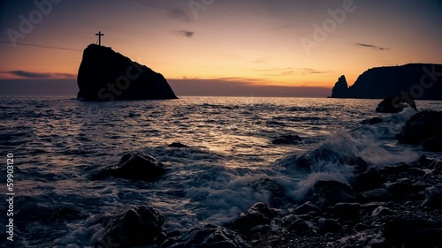 Cross on a rock in the sea, on the coast in the evening