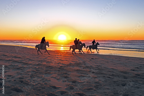 Horse riding on the beach at sunset