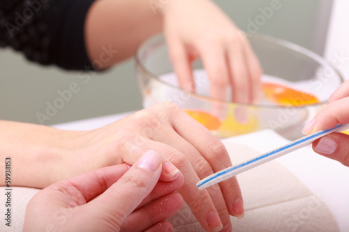 Beautician with file filing nails female client in beauty salon