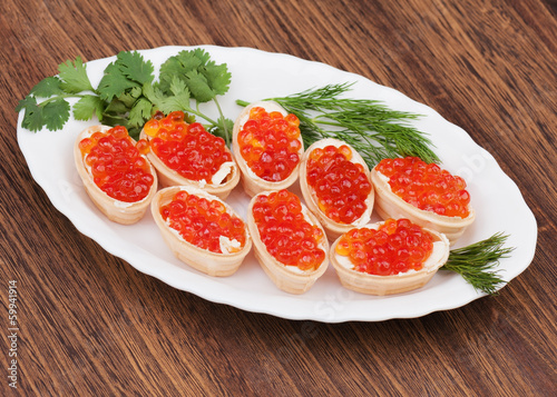 Tartlets with red caviar on wooden background.