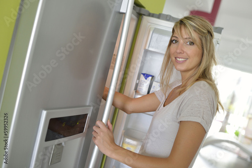 Smiling young woman opening fridge