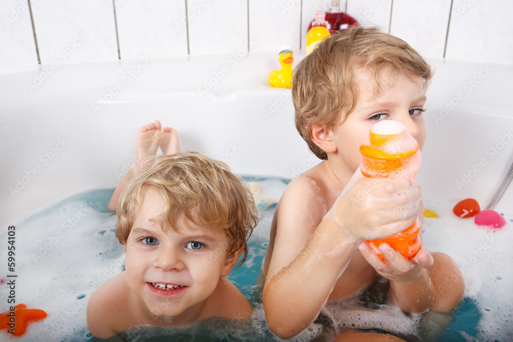 Two little twins boys having fun with water by taking bath in ba Two little twins boys having fun with water by taking bath in ba