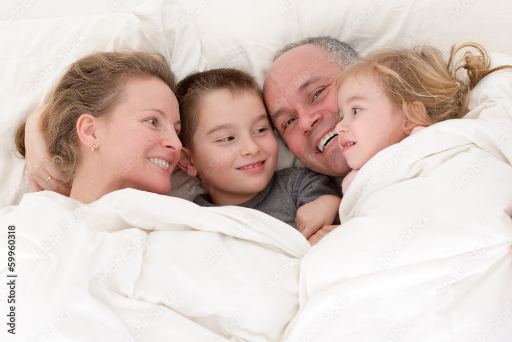 Happy young family cuddling together in bed