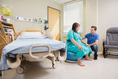 Man Looking At Pregnant Wife On Exercise Ball In Hospital