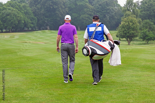 Golfer and caddy walking up a fairway photo