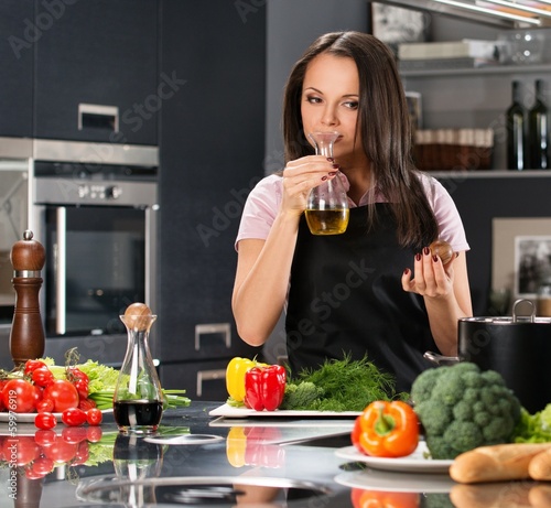 Young woman in apron on modern kitchen smelling olive oil