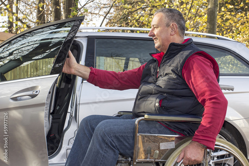 Man in a wheelchair in the fall next to their car photo