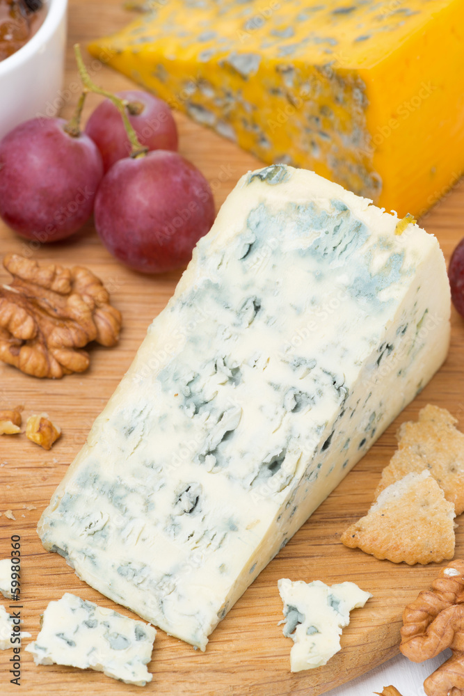 blue cheese, grapes, crackers, jam and nuts on a wooden board