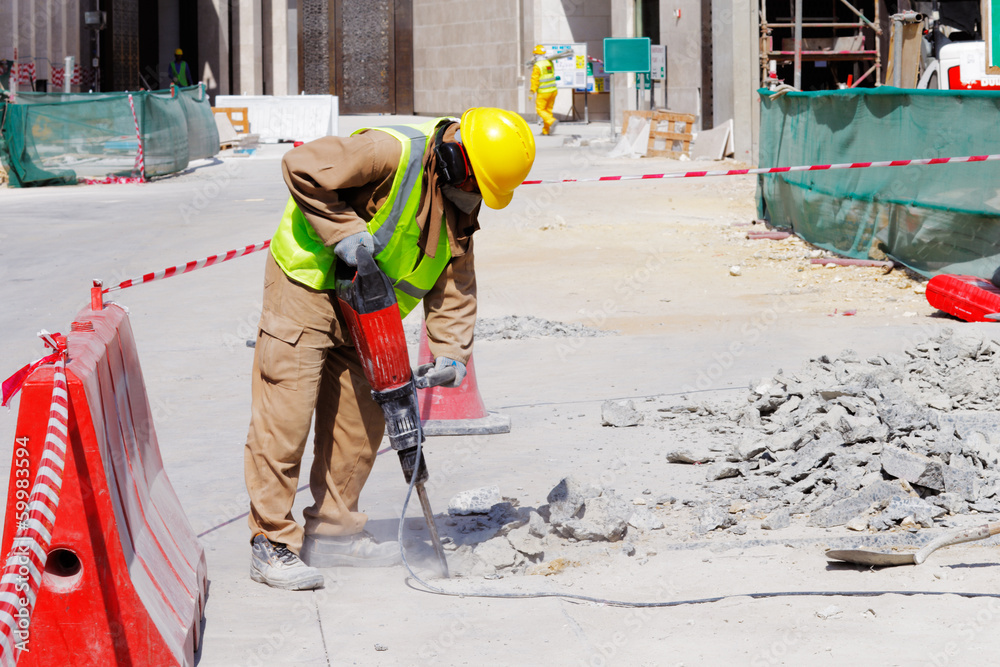 A laborer uses a jackhammer to break up a concrete pavement - obrazy, fototapety, plakaty 