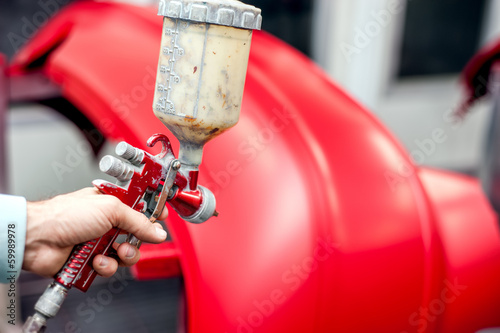 Close-up of spray gun with red paint painting a car
