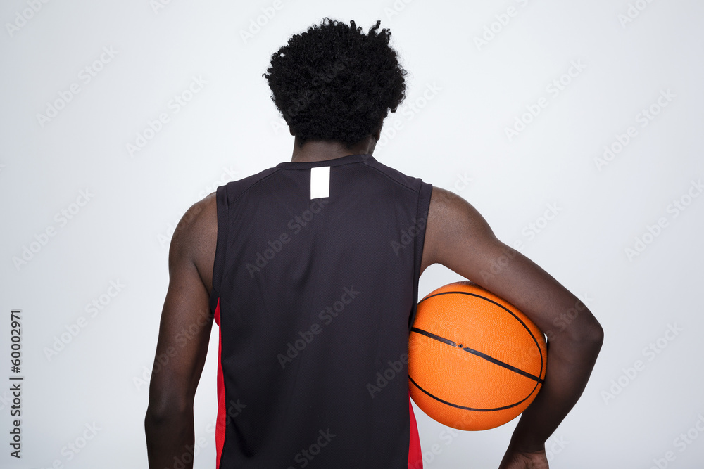 Back view of a basketball player holding a ball against gray bac - obrazy, fototapety, plakaty 