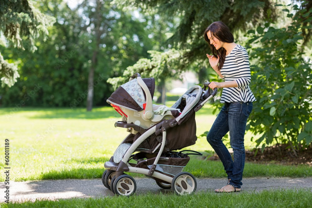 Woman Looking Into Baby Carriage In Park Woman Looking Into Baby Carriage In Park