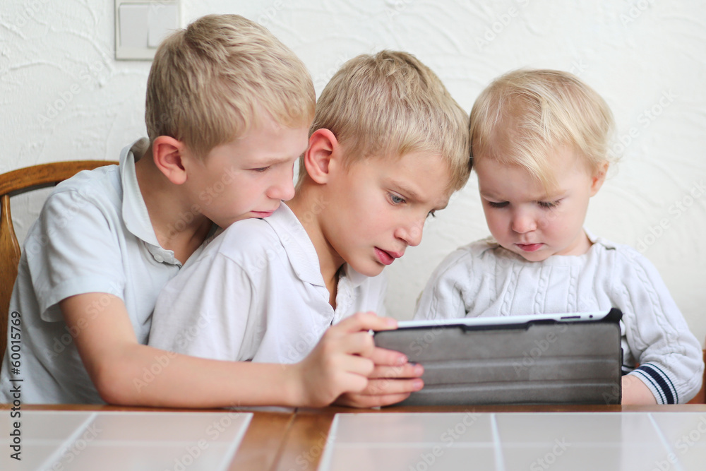 two twin brothers with cute toddler sister playing on a tablet two twin brothers with cute toddler sister playing on a tablet
