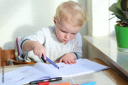 blonde toddler girl drawing family while sitting indoors