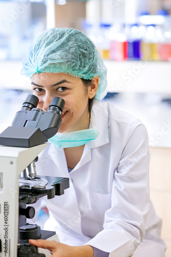 Friendly female lab technician using a microscope.