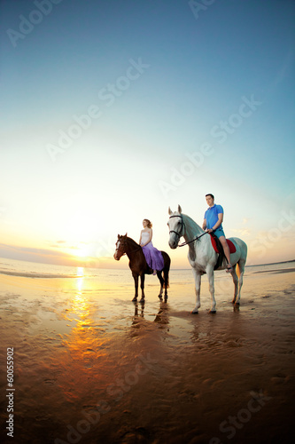 Two riders on horseback at sunset on the beach. Lovers ride hors