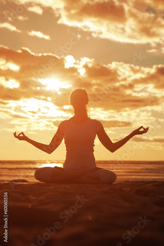 Young beautiful slim woman silhouette practices yoga on the beac