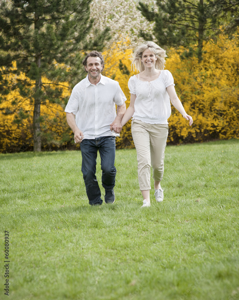 Fototapeta premium Couple running through park holding hands