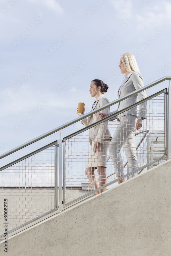 Side view of businesswomen moving down stairs against sky