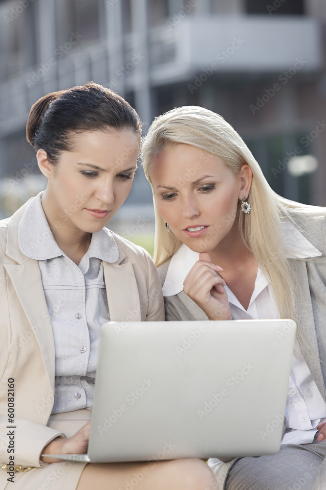 Young businesswomen working on laptop together while sitting outdoors Young businesswomen working on laptop together while sitting outdoors