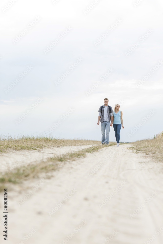 Full length of young hiking couple walking on path at field