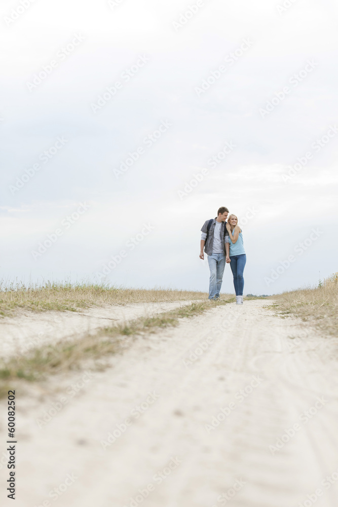 Full length of young hiking couple embracing while standing on path at field