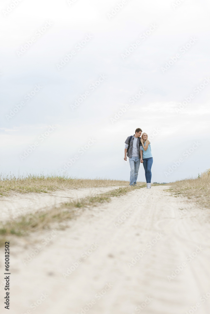 Full length of young hiking couple embracing while standing on path at field Full length of young hiking couple embracing while standing on path at field