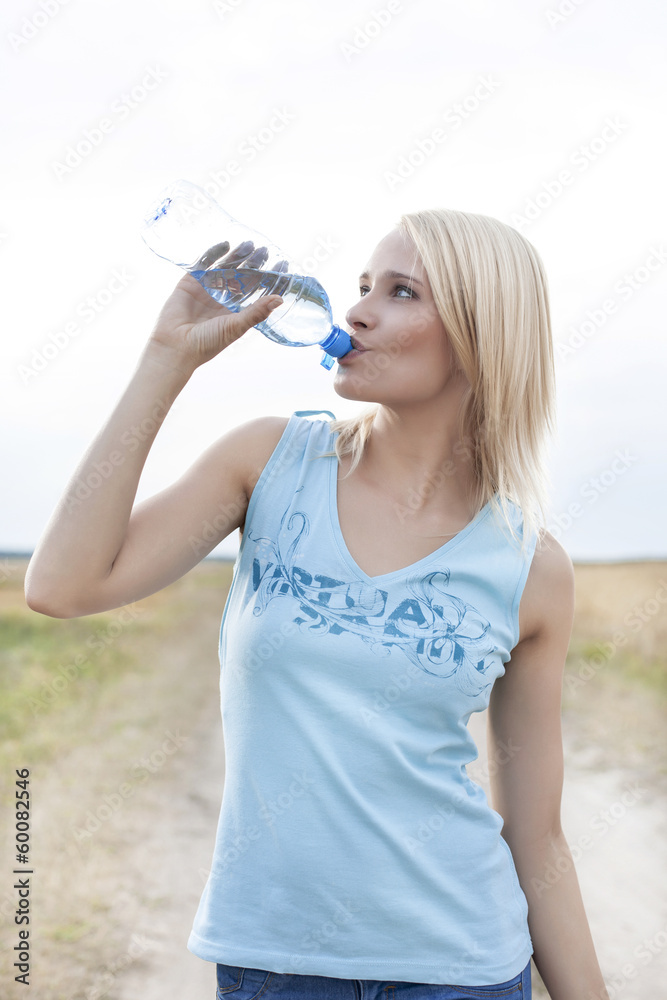 Young woman drinking water from bottle on field Young woman drinking water from bottle on field