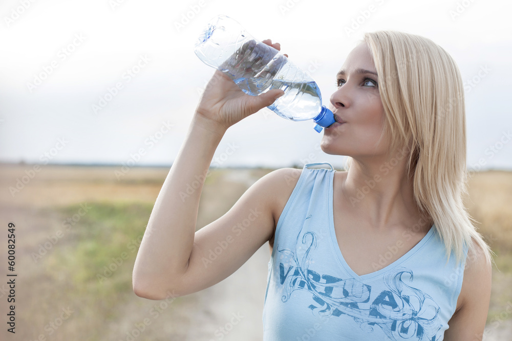 Beautiful woman drinking water from bottle while standing on field Beautiful woman drinking water from bottle while standing on field