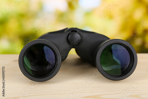 Black modern binoculars on wooden table on green background