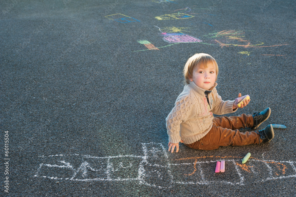 Naklejka premium Cute toddler boy drawing with chalk on a nice day outdoors