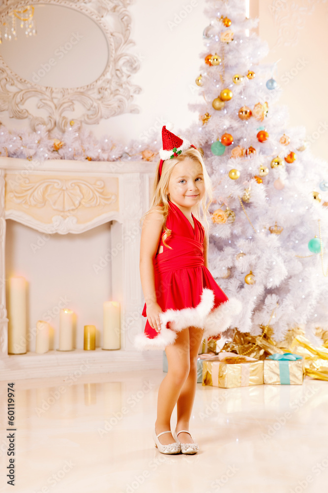 Beautiful little Santa girl near the Christmas tree.  Happy girl