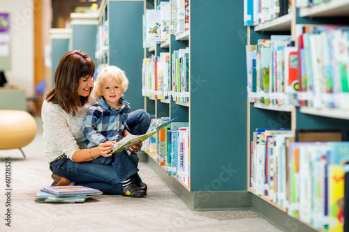 Boy With Teacher Reading Book In Library
