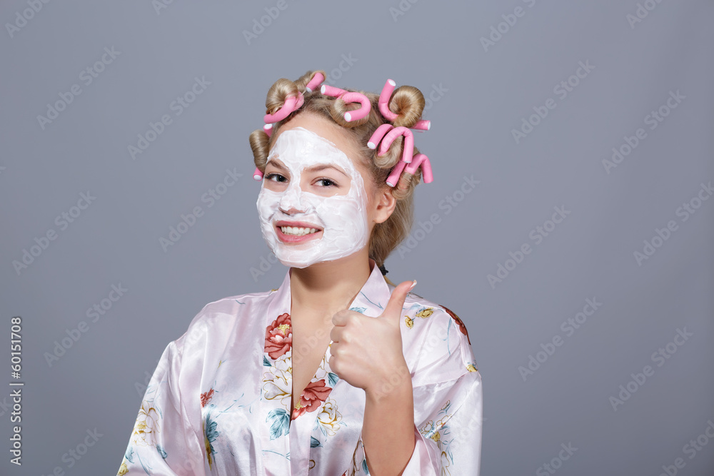 Girl in a cosmetic mask and curlers showing thumbs up Girl in a cosmetic mask and curlers showing thumbs up