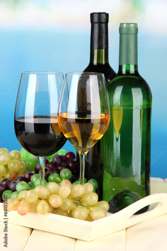 Fototapeta premium Wine bottles and glasses of wine on tray, on bright background