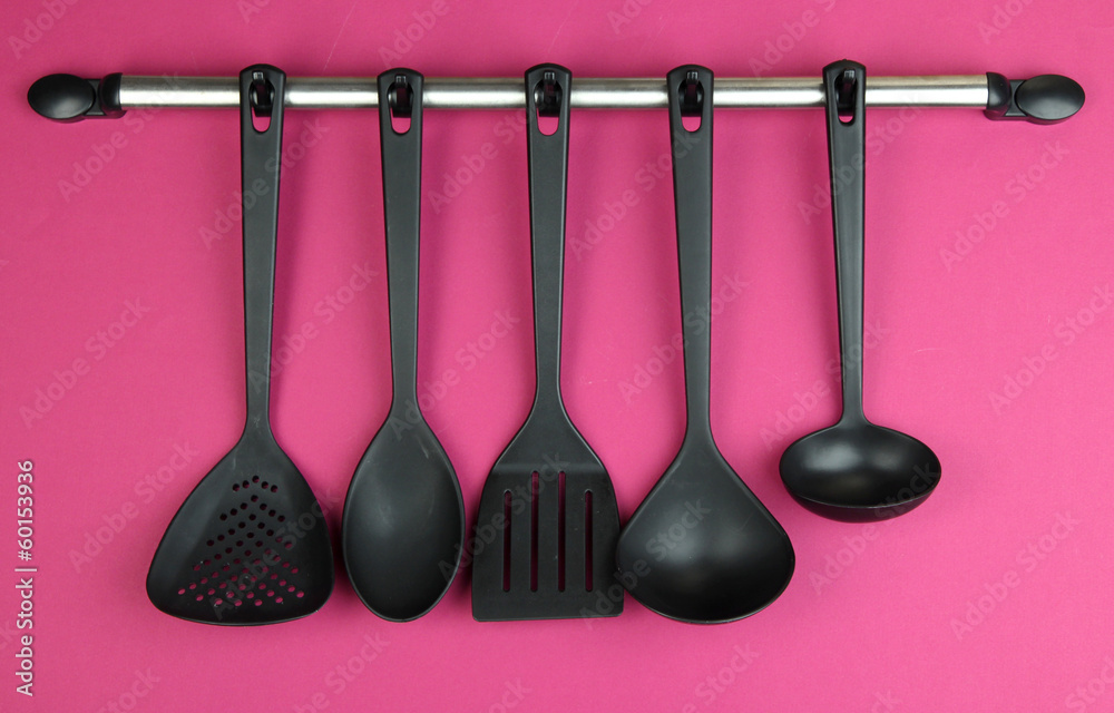 Plastic kitchen utensils on silver hooks on red background Plastic kitchen utensils on silver hooks on red background