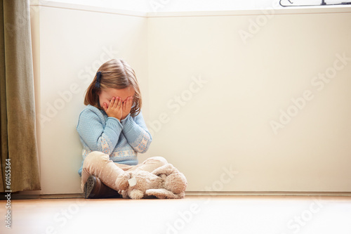 Unhappy Child Sitting On Floor In Corner At Home photo
