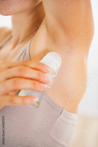 Closeup on young woman applying deodorant on underarm