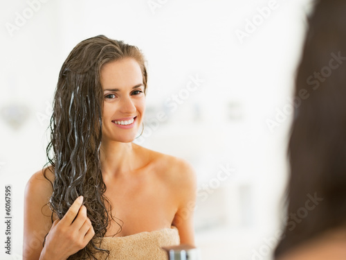 Happy young woman applying hair mask in bathroom photo