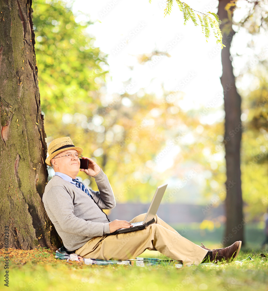 Senior man sitting in a park, talking on a phone and working on Senior man sitting in a park, talking on a phone and working on