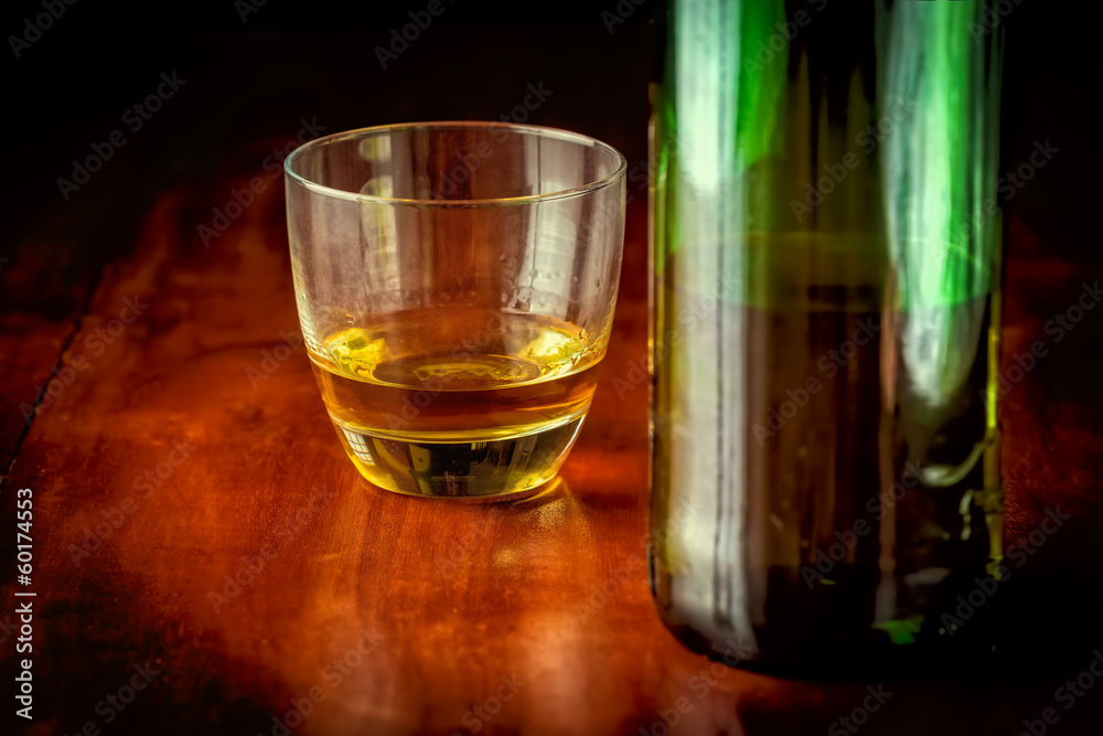 Glass of scotch and a green liquor bottle on a wooden table