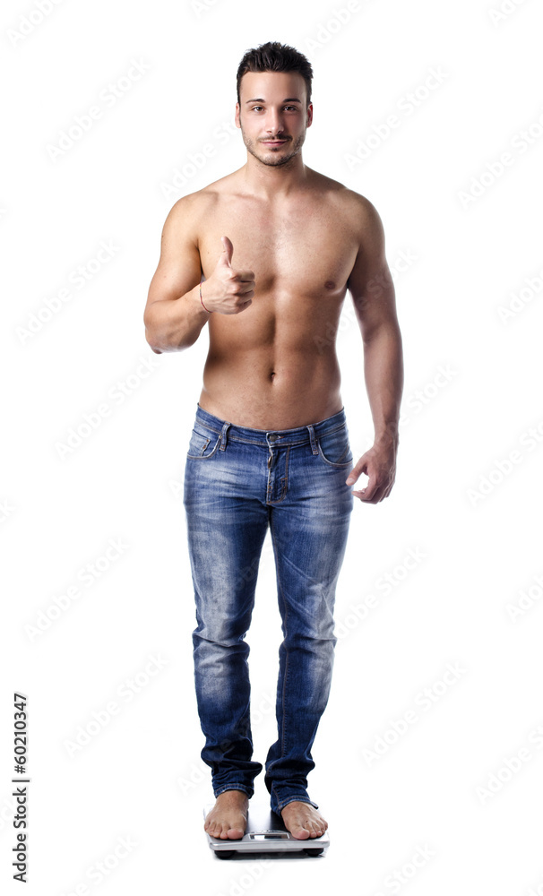 Muscular young man weighing himself on scale, making OK sign Muscular young man weighing himself on scale, making OK sign