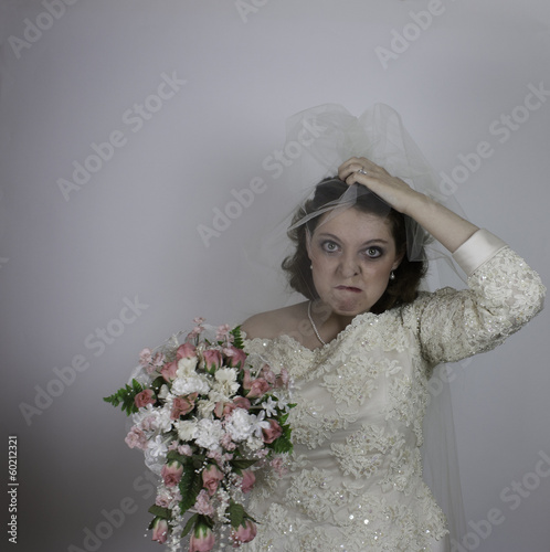 Pretty young bride frowning and holding up her veil photo