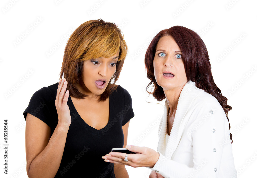 Two shocked women looking at phone seeing bad news or photos Two shocked women looking at phone seeing bad news or photos