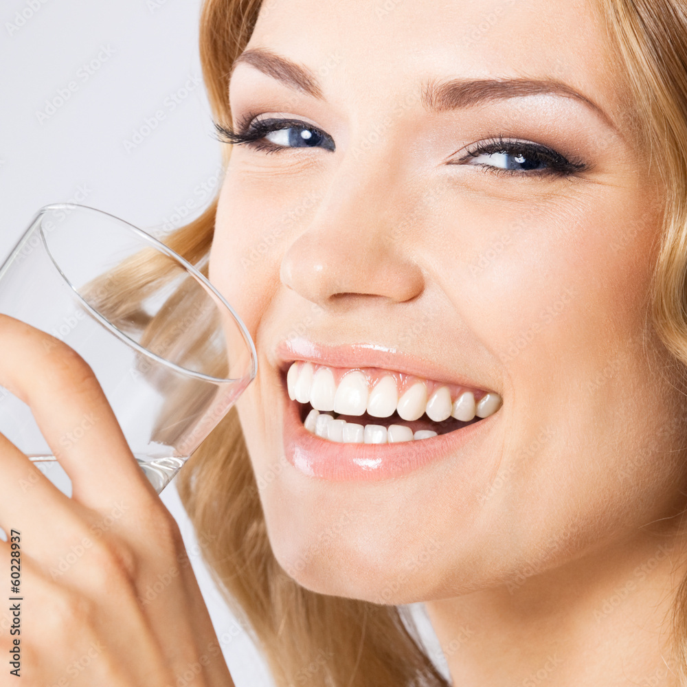 Fototapeta premium Young woman drinking water, on gray