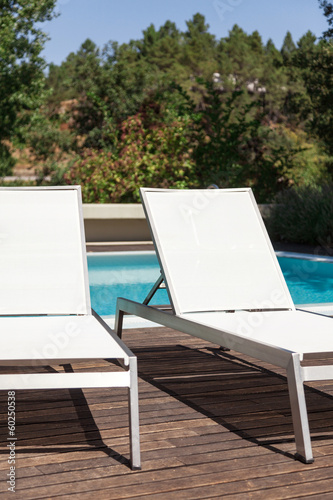 White loungers near a pool with trees in background © Luis Viegas