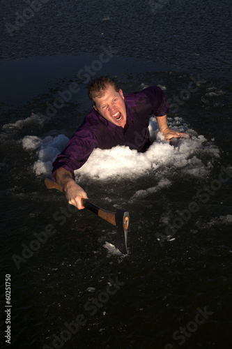 man in ice hole climbing out holding axe